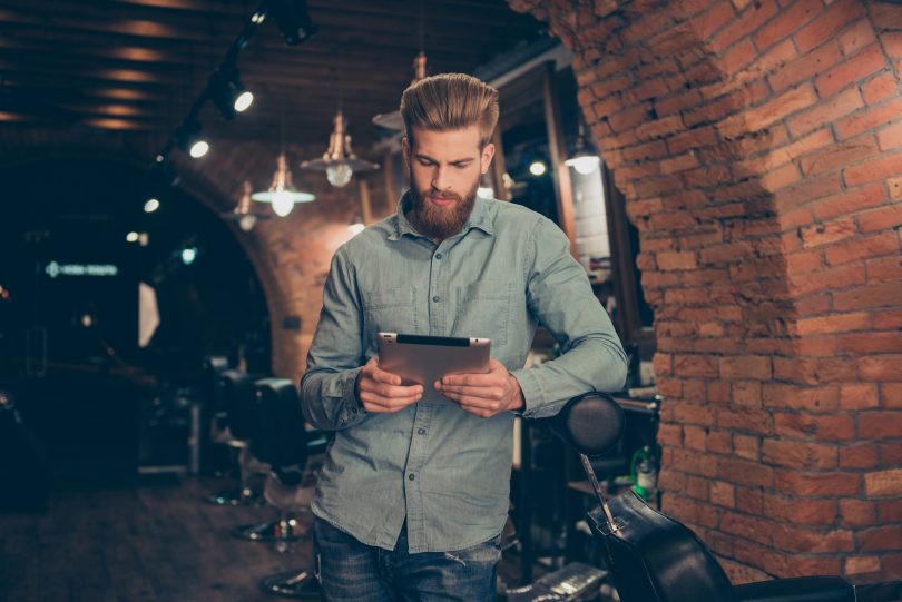 Male barber in barber shop looking at tablet