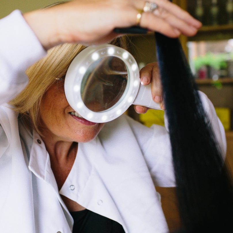 Eva Proudman Consultant Trichologist inspecting hair with light up magnifying glass